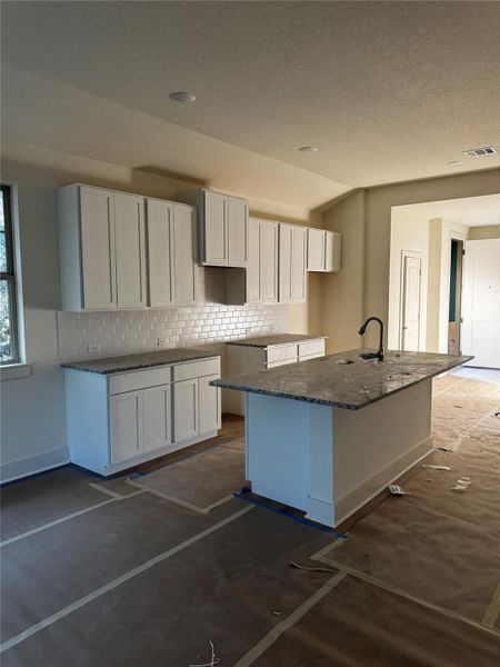 Kitchen with white cabinetry, tasteful backsplash, a kitchen island with sink, dark stone countertops, and a breakfast bar area