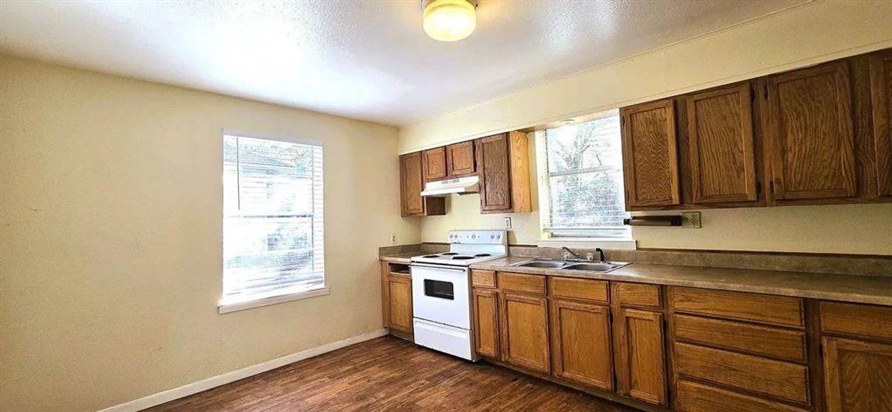Kitchen featuring white electric range oven, healthy amount of natural light, dark wood-style floors, and under cabinet range hood
