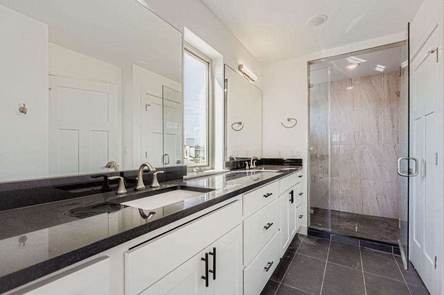 Bathroom featuring double vanity, a stall shower, and dark tile patterned floors