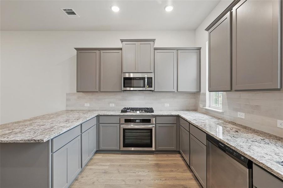 Kitchen featuring gray cabinets, light wood-type flooring, stainless steel appliances, a peninsula, and light stone countertops