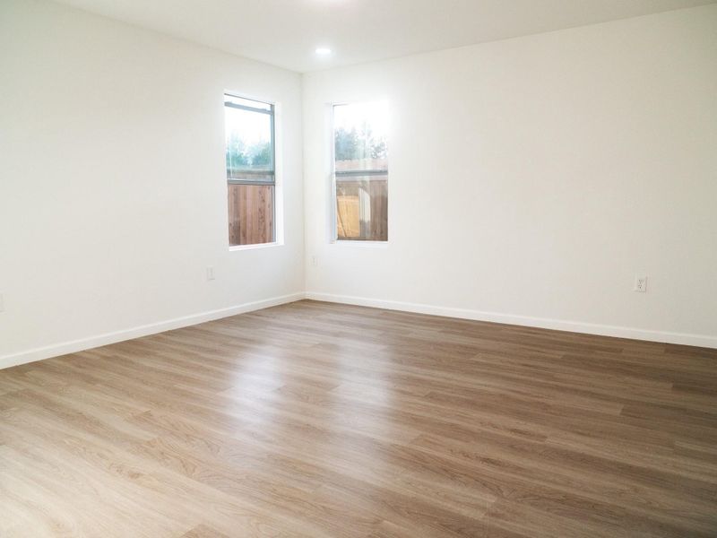 Bright, spacious room with white walls and wood-style flooring. Two large windows provide natural light, ideal for a cozy living area or bedroom.
