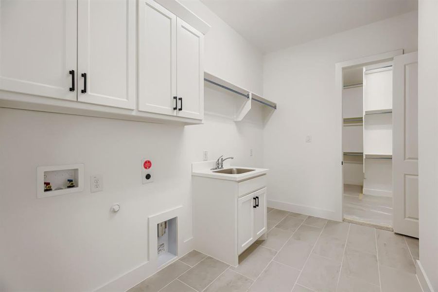 Utility room featuring white shaker cabinetry, an integrated utility sink, overhead shelving, and neutral tile flooring Utility room featuring white shaker cabinetry, an integrated utility sink, overhead shelving, and neutral tile flooring