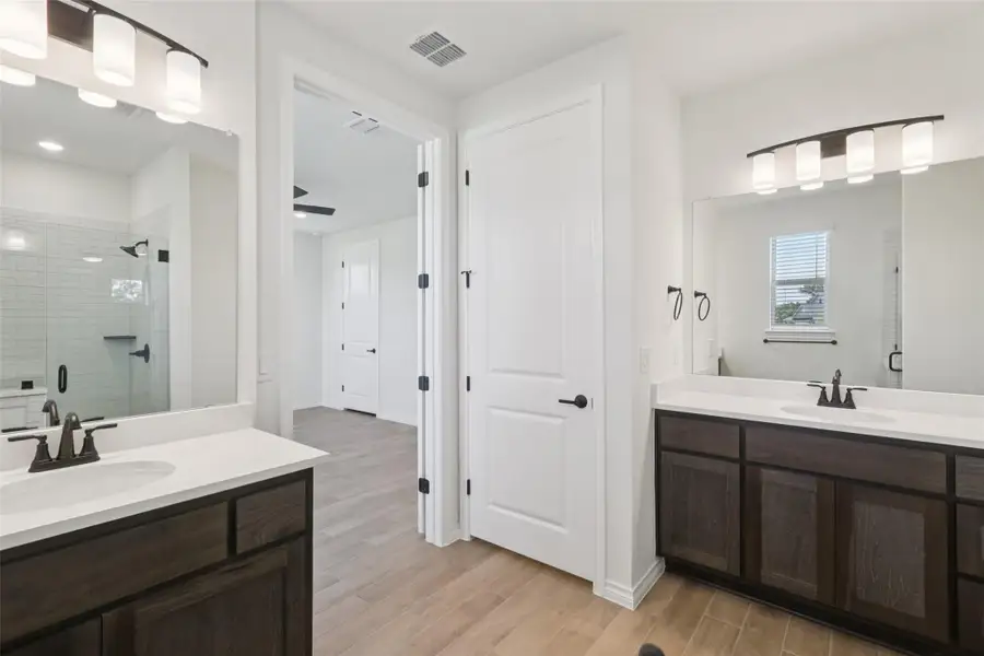 Full bath featuring a shower stall, two vanities, and wood finished floors