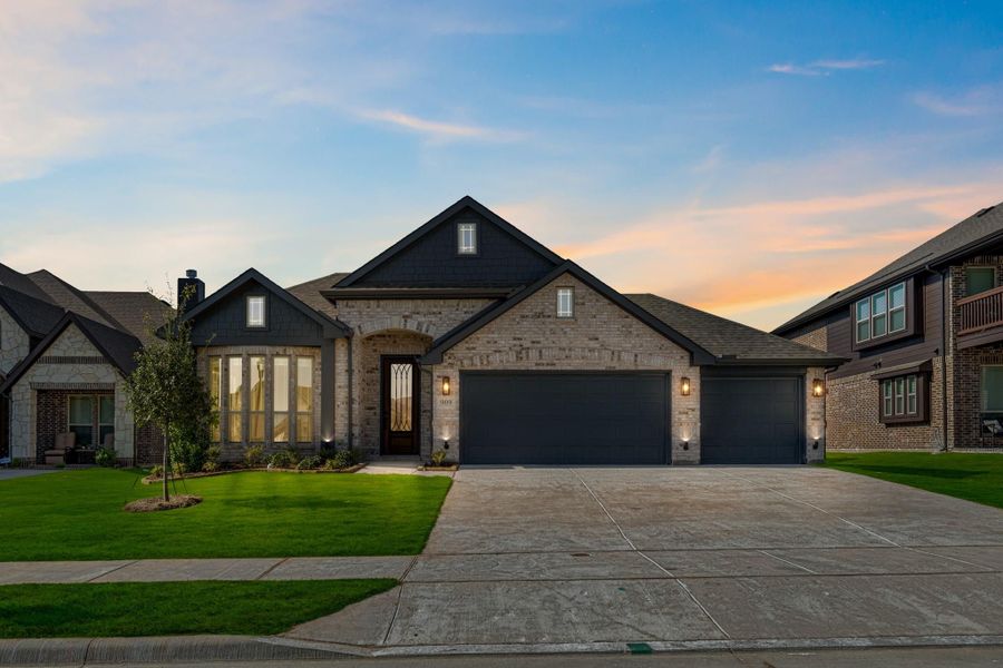 Single-story brick home with dark trim, two-car garage, arched entry, and manicured front lawn at dusk.