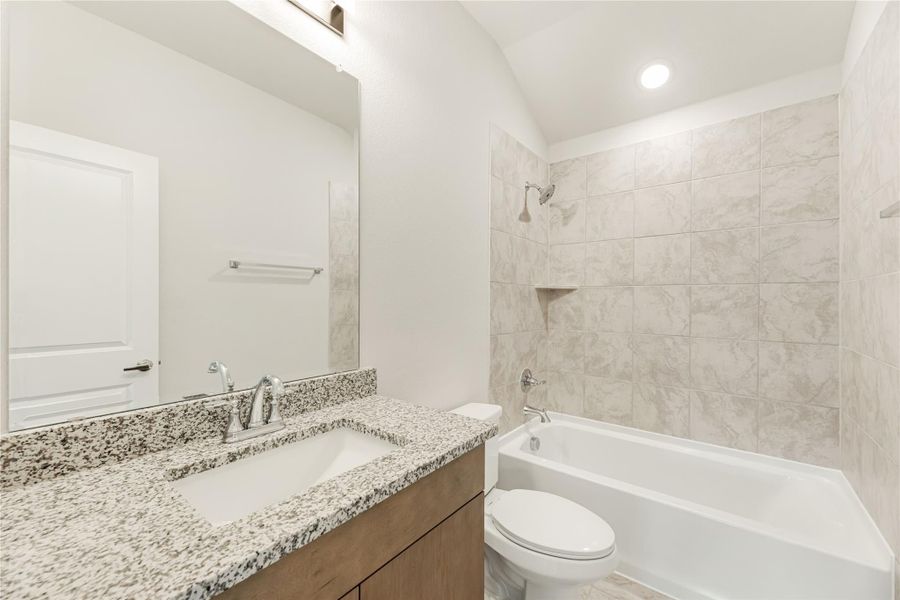 Bathroom with granite countertop vanity, toilet, and tiled tub-shower combo with vaulted ceiling