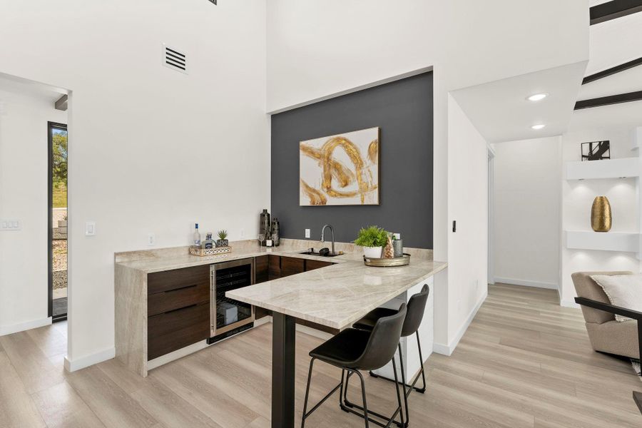 Indoor wet bar with light stone countertops, light wood-type flooring, wine cooler, modern cabinets, and a high ceiling
