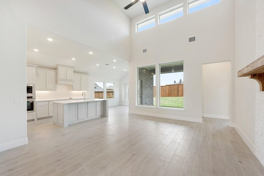 Open-concept living area with two-story ceiling, light wood floors, and kitchen island with white cabinets visible in background.