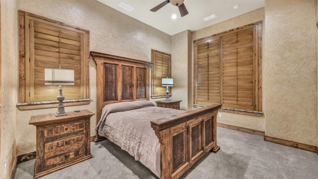 Comfortable guest bedroom with plush carpeting, wood-framed windows, and neutral tones.
