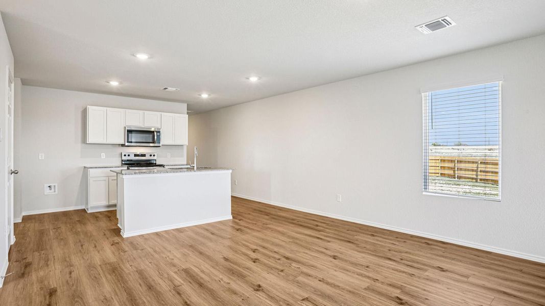 Open-concept kitchen and living area featuring wood-finish flooring, white cabinetry, a kitchen island with sink, and recessed lighting Open-concept kitchen and living area featuring wood-finish flooring, white cabinetry, a kitchen island with sink, and recessed lighting