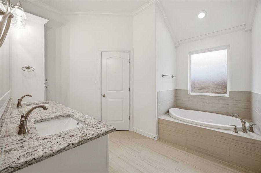 This bathroom features a double vanity with granite countertops and two sinks, a built-in bathtub, and tiled flooring