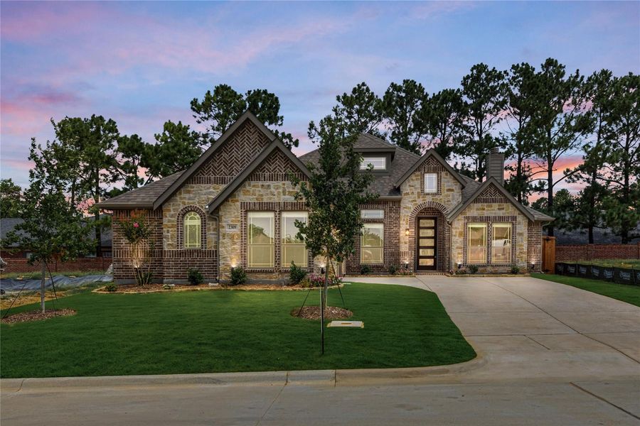 Single-story home with brick and stone exterior, arched entry, large windows, and curved driveway at dusk
