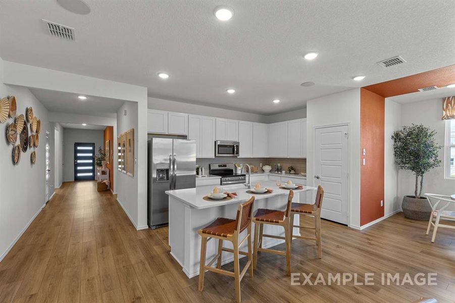 Kitchen with a center island with sink, appliances with stainless steel finishes, light hardwood / wood-style floors, white cabinetry, and a breakfast bar area