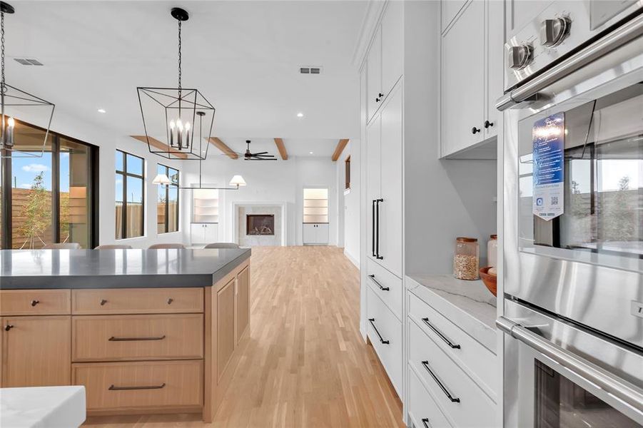 Kitchen with double oven, a fireplace, ceiling fan, light wood finish cabinetry, and light wood-style floors Kitchen with double oven, a fireplace, ceiling fan, light wood finish cabinetry, and light wood-style floors