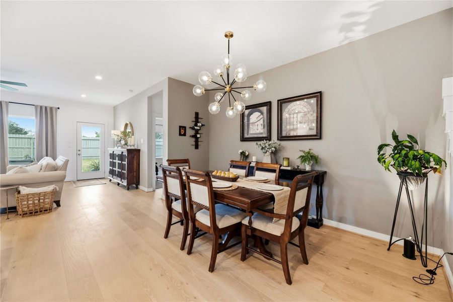 Dining room with upgraded designer lighting, a custom accent wall and hardwood flooring.