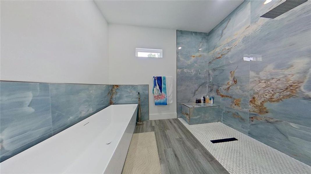 Contemporary bathroom featuring a freestanding soaking tub, expansive blue-hued stone-look tile, wood-finish flooring, a walk-in shower with a built-in bench, and a small transom window Contemporary bathroom featuring a freestanding soaking tub, expansive blue-hued stone-look tile, wood-finish flooring, a walk-in shower with a built-in bench, and a small transom window