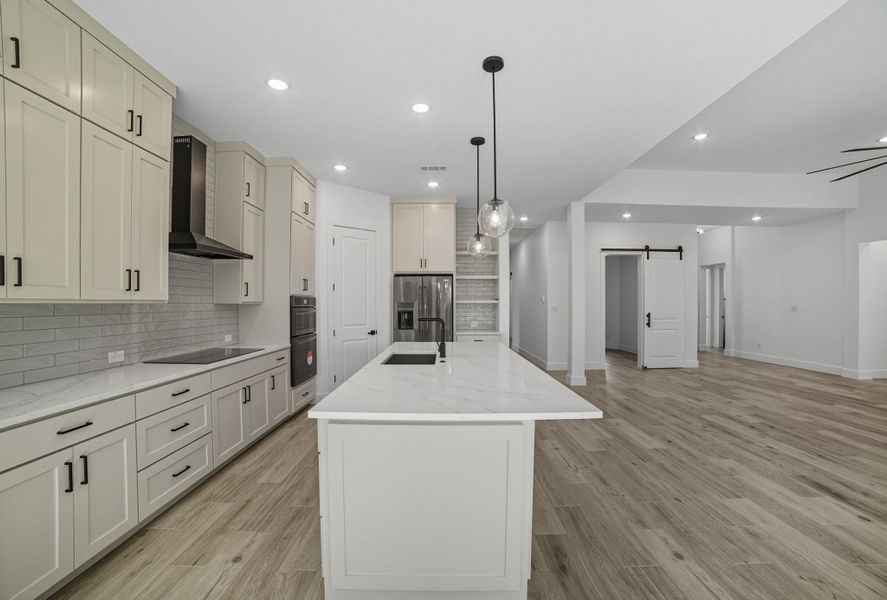Kitchen featuring a barn door, backsplash, light stone countertops, pendant lighting, and recessed lighting Kitchen featuring a barn door, backsplash, light stone countertops, pendant lighting, and recessed lighting