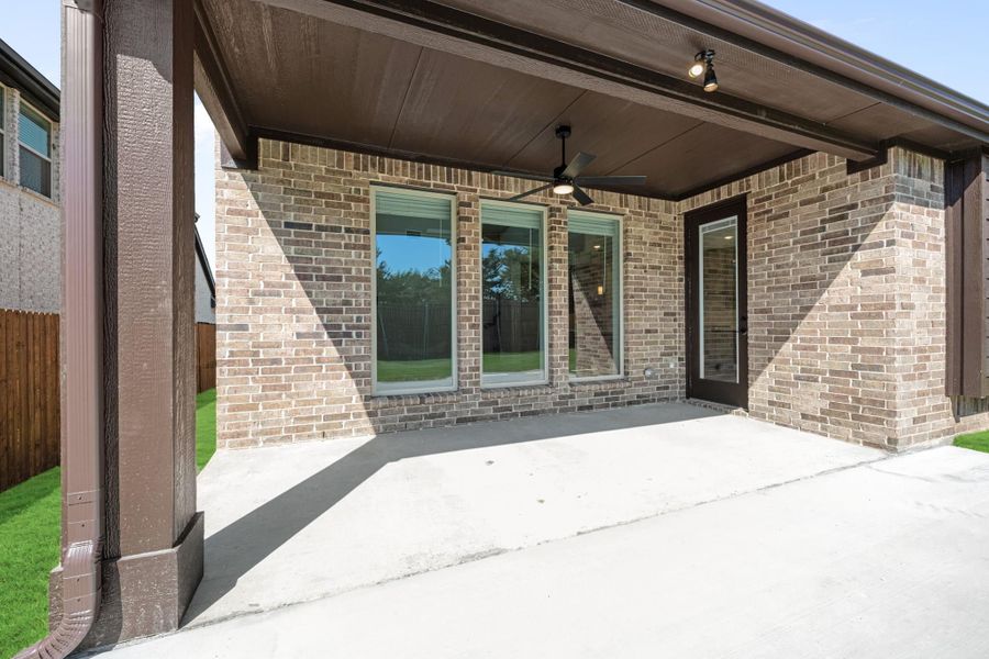 Covered back patio with ceiling fan, brick exterior, sliding glass door, and concrete floor