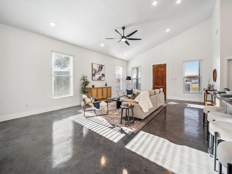 Living room with ceiling fan, plenty of natural light, and high vaulted ceiling