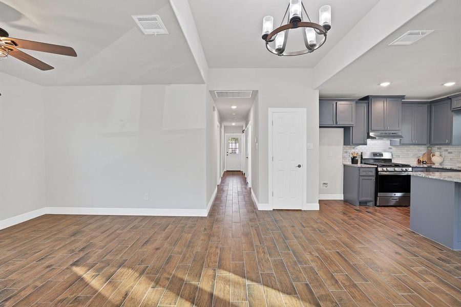 Kitchen with dark wood-type flooring, stainless steel gas stove, decorative backsplash, and gray cabinetry