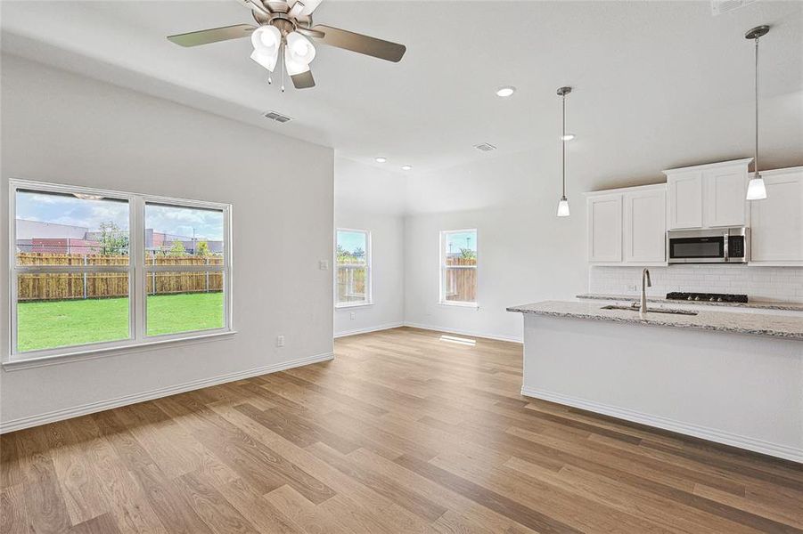 Kitchen with light stone countertops, sink, decorative backsplash, light wood-type flooring, and white cabinets