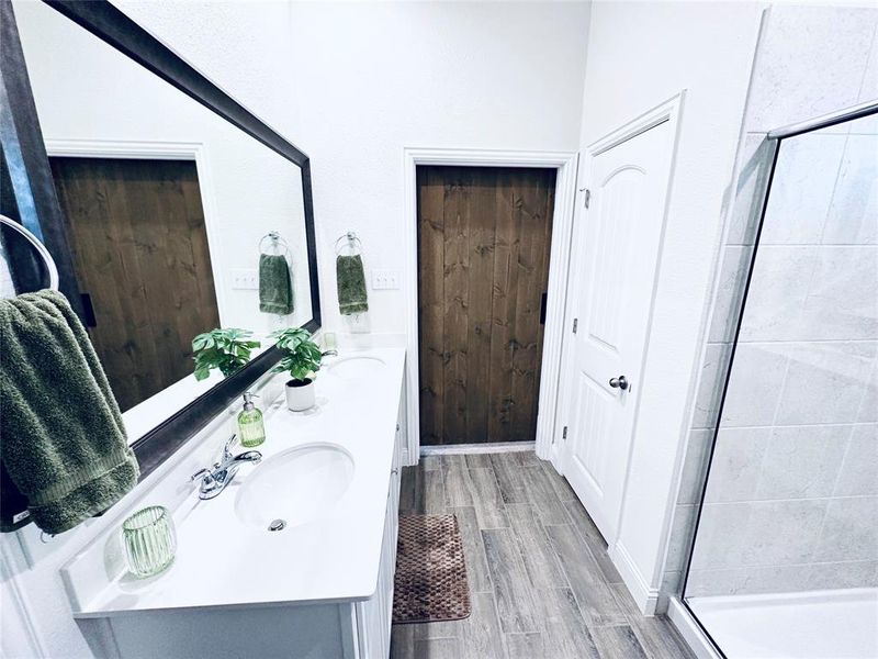 Bathroom with dual vanity, hardwood / wood-style flooring, and an enclosed shower