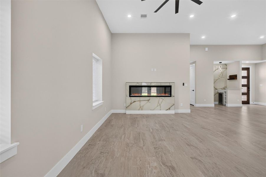 Spacious living area with elegant wood flooring, a modern electric fireplace, and abundant natural light.