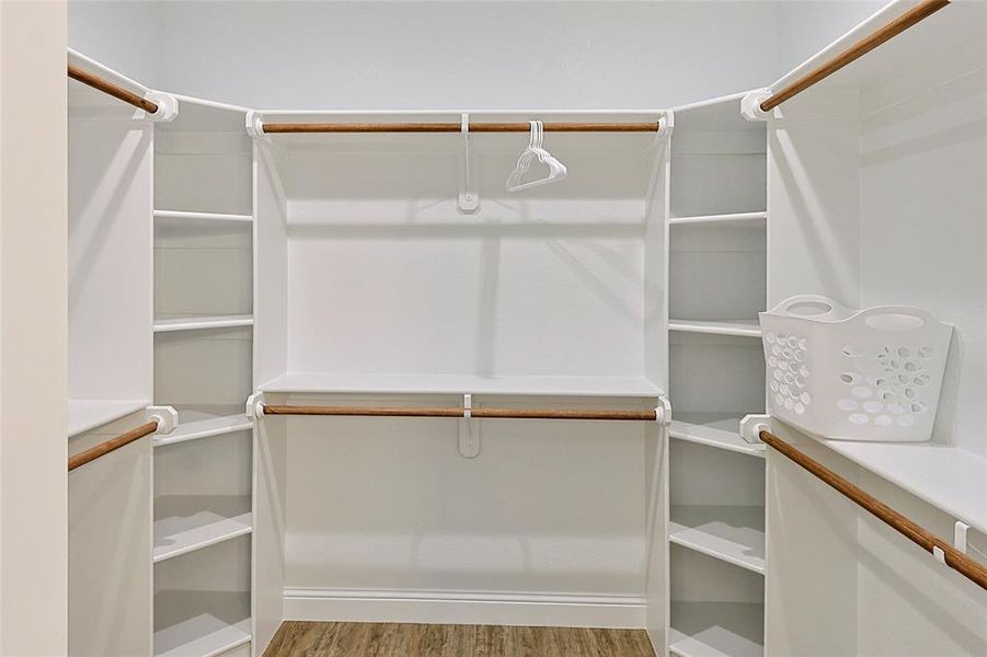 Spacious walk-in closet featuring white built-in shelving, multiple hanging rods, and wood-finish flooring