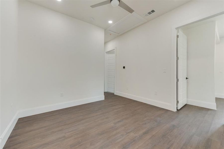 Spacious room featuring wood-finish flooring, recessed lighting, a contemporary ceiling fan, white baseboards, and a white paneled door Spacious room featuring wood-finish flooring, recessed lighting, a contemporary ceiling fan, white baseboards, and a white paneled door