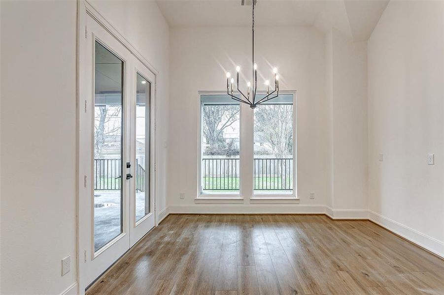 The breakfast room is ideal for circle table dining for 4 and features hardwood flooring, designer paint, a tall ceiling, a chic chandelier, easy backyard access, and bright windows.