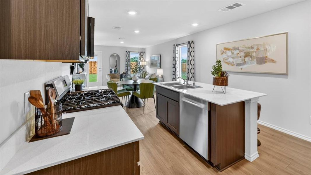 Modern kitchen featuring a gas range, white countertops, dark wood-finish cabinetry, stainless steel appliances, and wood-finish flooring Modern kitchen featuring a gas range, white countertops, dark wood-finish cabinetry, stainless steel appliances, and wood-finish flooring