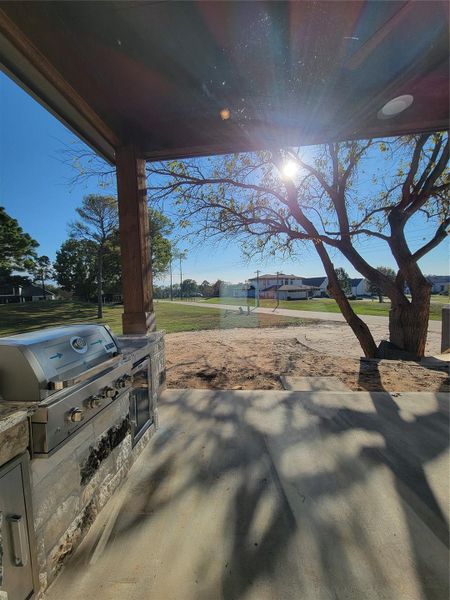 Spacious outdoor patio area with a built-in grill, overlooking a scenic view of a golf course. The space is shaded by a tree and framed by a wooden structure, offering a serene setting perfect for outdoor entertaining. Spacious outdoor patio area with a built-in grill, overlooking a scenic view of a golf course. The space is shaded by a tree and framed by a wooden structure, offering a serene setting perfect for outdoor entertaining.