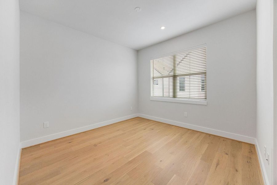 Bright secondary bedroom featuring hardwood floors, large windows, and a flexible layout ideal for guests, a home office, or additional living space.