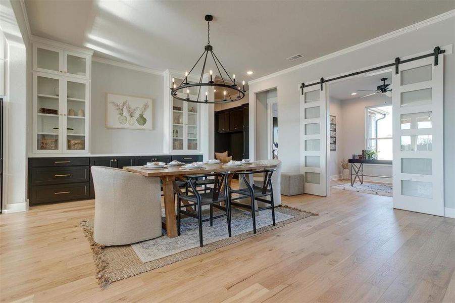 Dining space featuring a barn door, crown molding, light hardwood / wood-style floors, and ceiling fan with notable chandelier