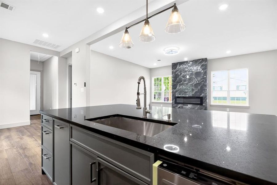 Kitchen with dark stone countertops, dark wood finished floors, open floor plan, hanging light fixtures, and gray cabinets Kitchen with dark stone countertops, dark wood finished floors, open floor plan, hanging light fixtures, and gray cabinets