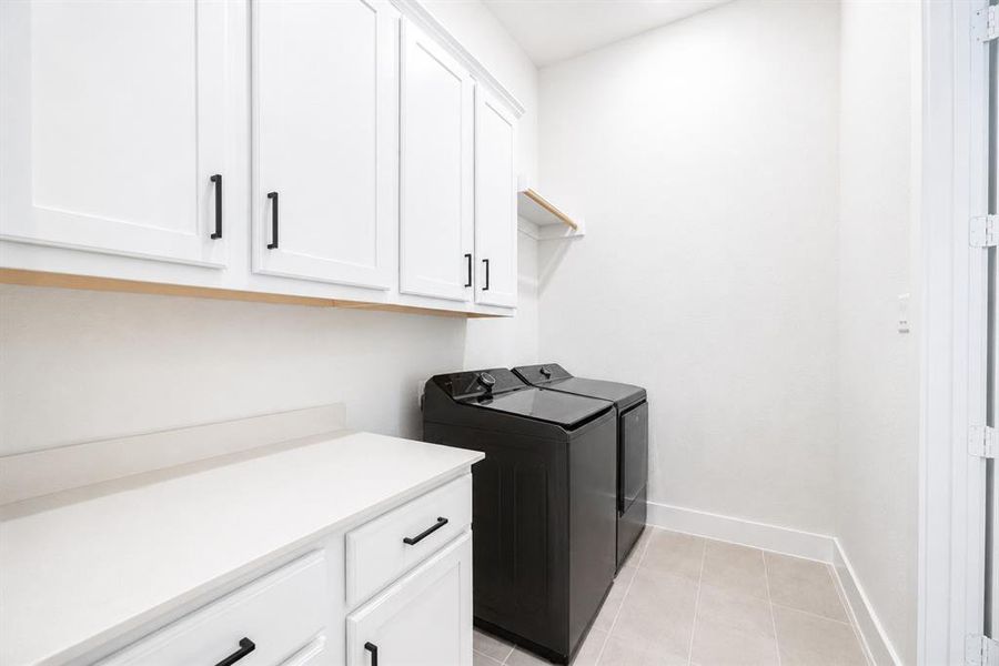 Laundry area featuring white shaker-style cabinetry with black hardware, white countertop space, and light-toned floor tiling