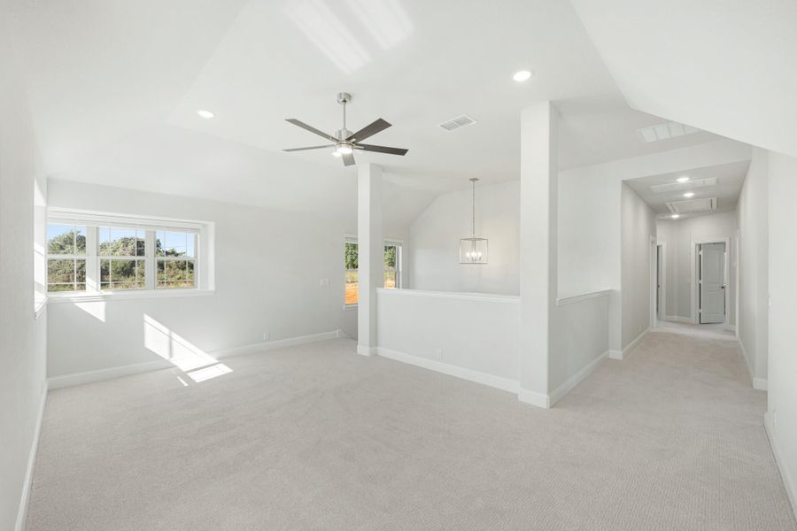 Spacious open room with vaulted ceiling, ceiling fan, carpet flooring, and hallway leading to additional rooms