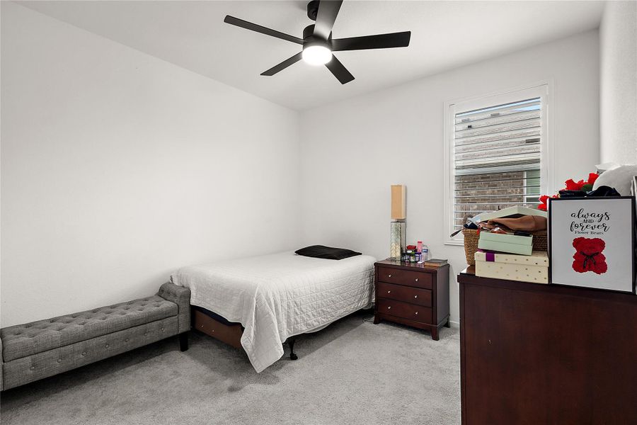 This cozy bedroom features a minimalist design with neutral colors, a ceiling fan, and a window for natural light. It includes a bed, a bench, and wooden dressers for storage.
