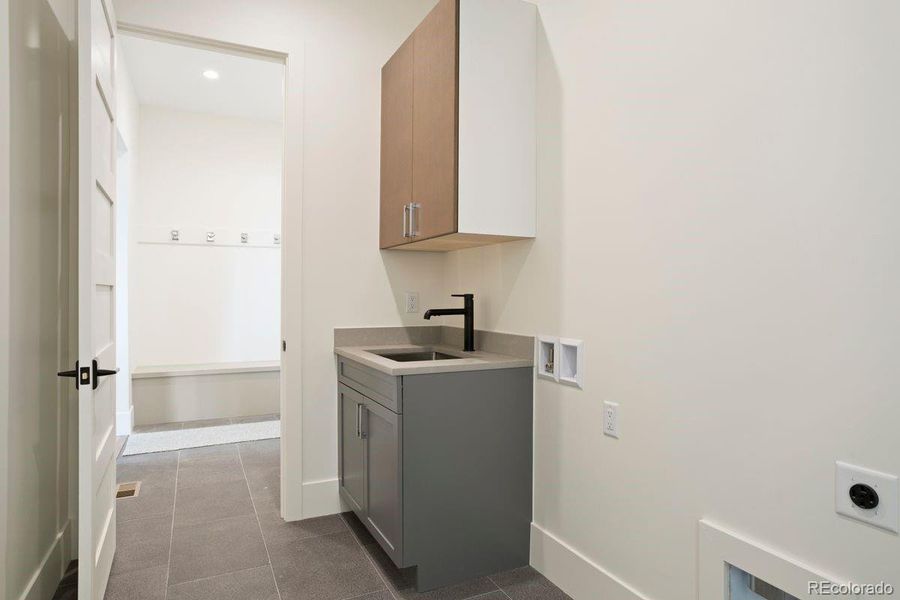 Laundry room with built-in cabinetry, utility sink, and durable tile flooring.