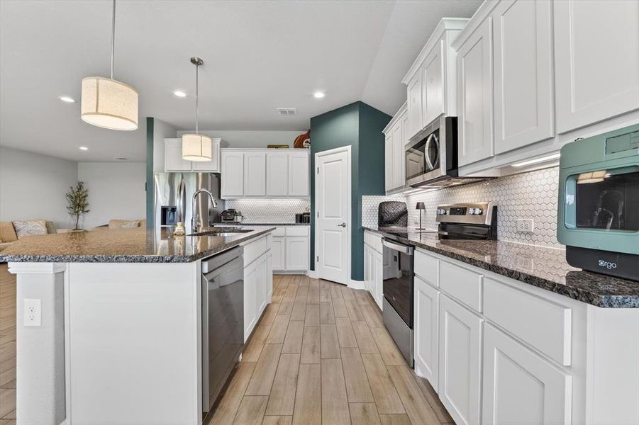Modern kitchen featuring white shaker cabinetry, stainless steel appliances, dark stone countertops, and a white penny tile backsplash