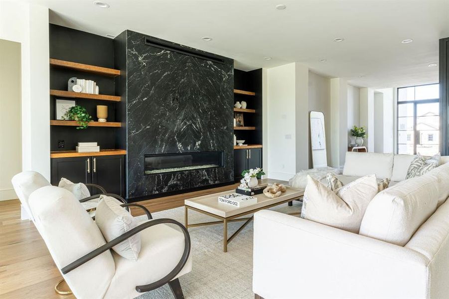 Living room featuring light hardwood / wood-style flooring, a high end fireplace, and built in shelves