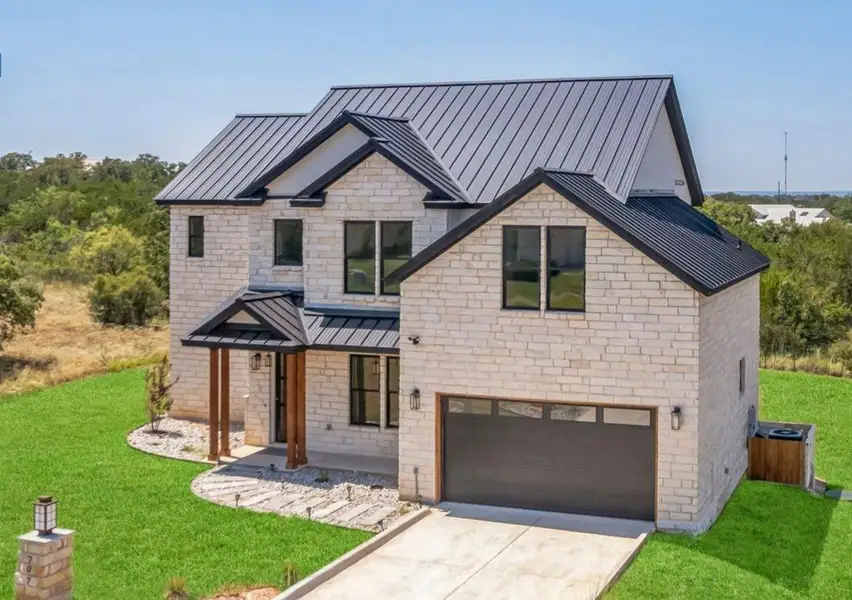 View of front facade featuring an attached garage, a standing seam roof, a front lawn, and metal roof View of front facade featuring an attached garage, a standing seam roof, a front lawn, and metal roof