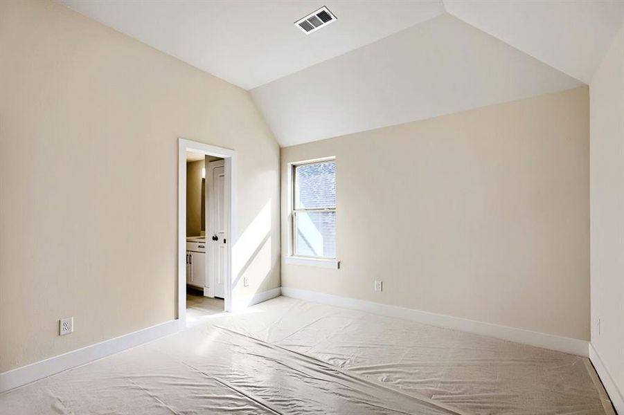 Unfurnished bedroom with vaulted ceiling, light colored carpet, and ensuite bathroom Unfurnished bedroom with vaulted ceiling, light colored carpet, and ensuite bathroom