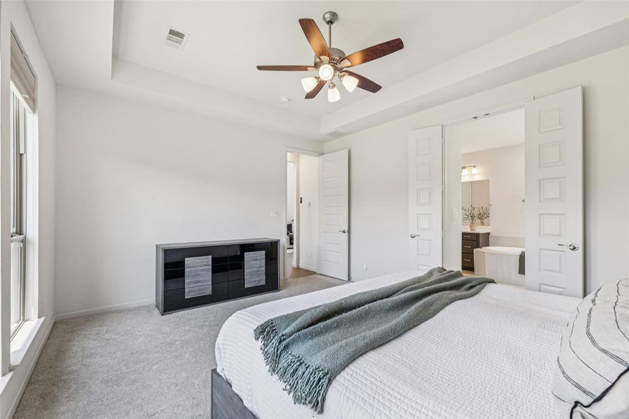 This room features light-colored walls and carpet, a ceiling fan with integrated lighting, and a large window