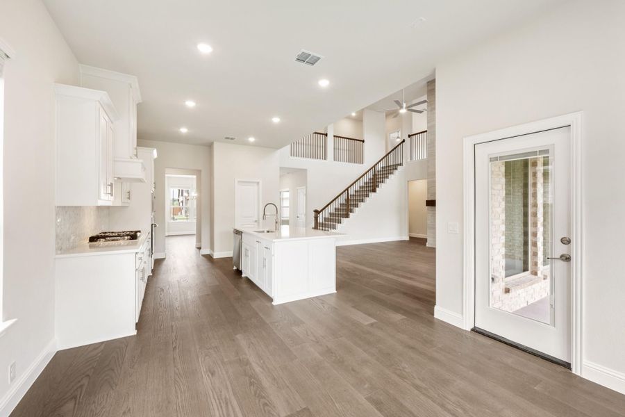 Open-concept living area with white kitchen island, hardwood floors, and staircase in background