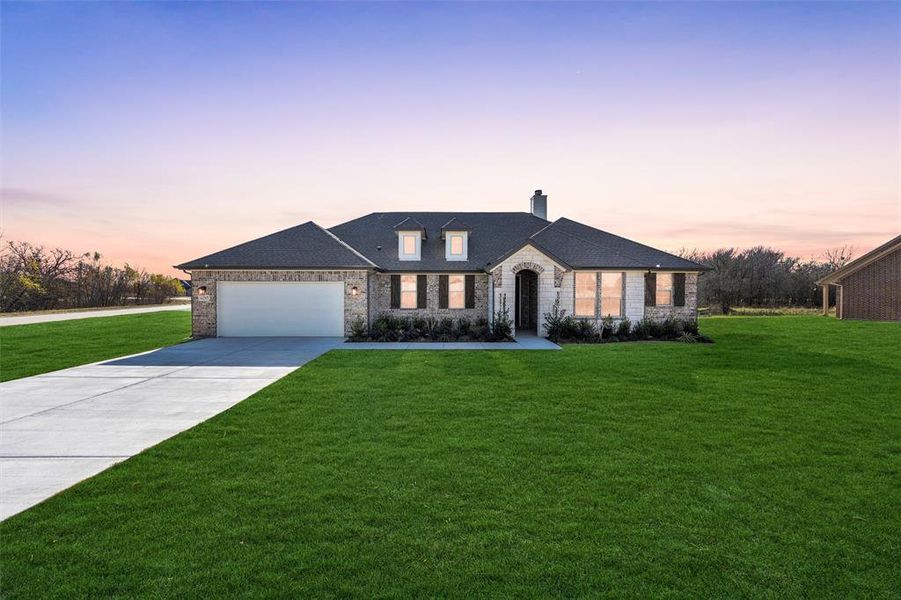French provincial home featuring a front lawn, a chimney, driveway, and stone siding