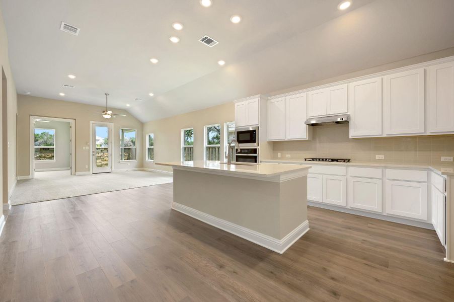 Kitchen with vaulted ceiling, recessed lighting, open floor plan, white cabinetry, and ceiling fan