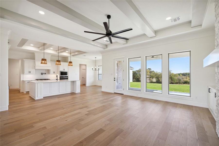 Unfurnished living room featuring beam ceiling, sink, a raised ceiling, ceiling fan with notable chandelier, and light wood-type flooring