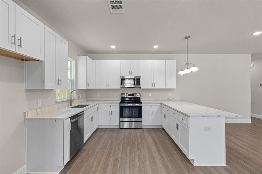 Kitchen with sink, white cabinets, kitchen peninsula, appliances with stainless steel finishes, and decorative light fixtures