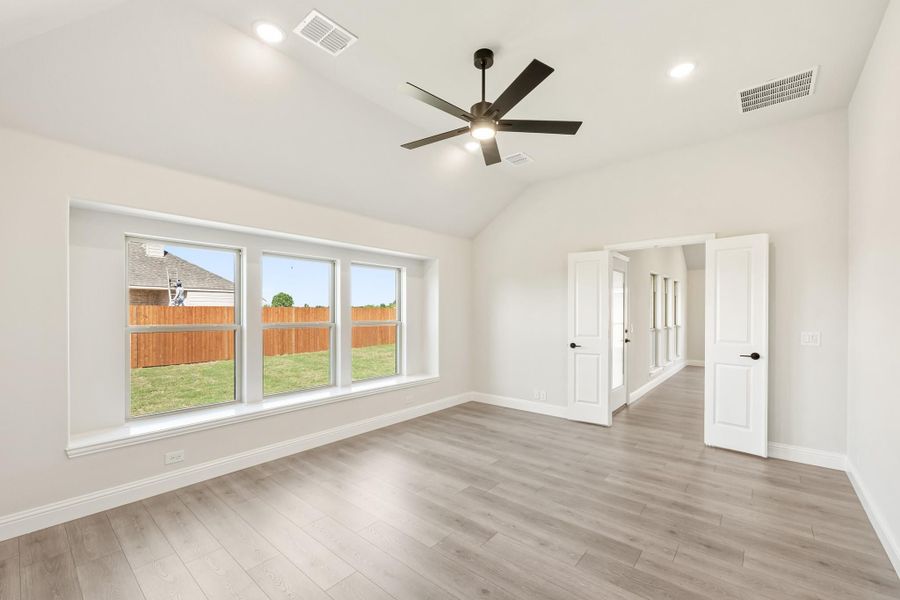 Empty bedroom with vaulted ceiling, ceiling fan, hardwood floors, and large windows overlooking backyard Empty bedroom with vaulted ceiling, ceiling fan, hardwood floors, and large windows overlooking backyard