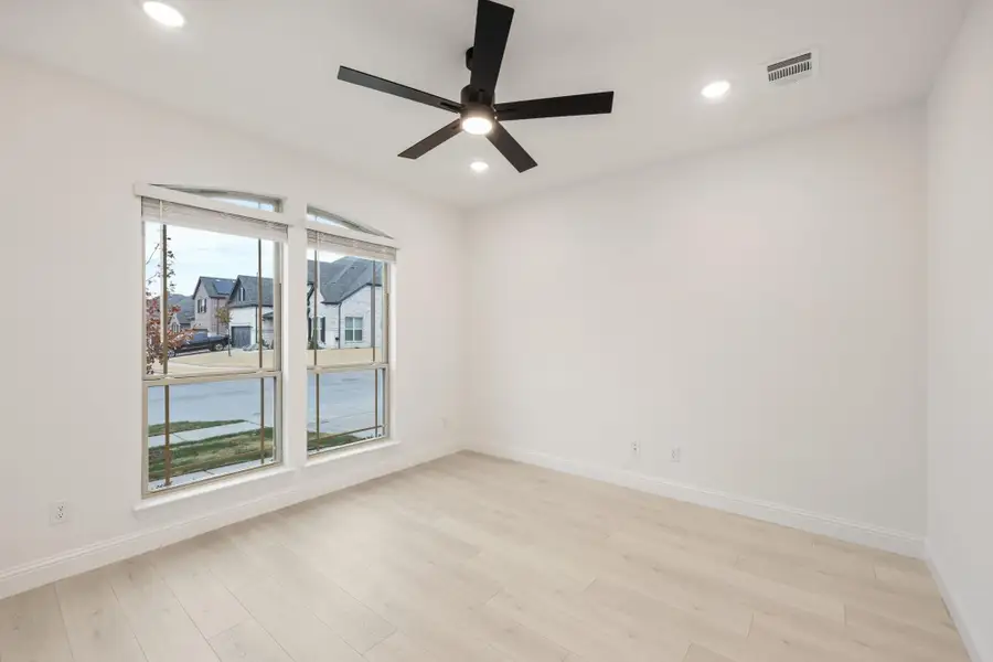 Empty room with light wood floors, black ceiling fan, and large windows overlooking a neighborhood street Empty room with light wood floors, black ceiling fan, and large windows overlooking a neighborhood street